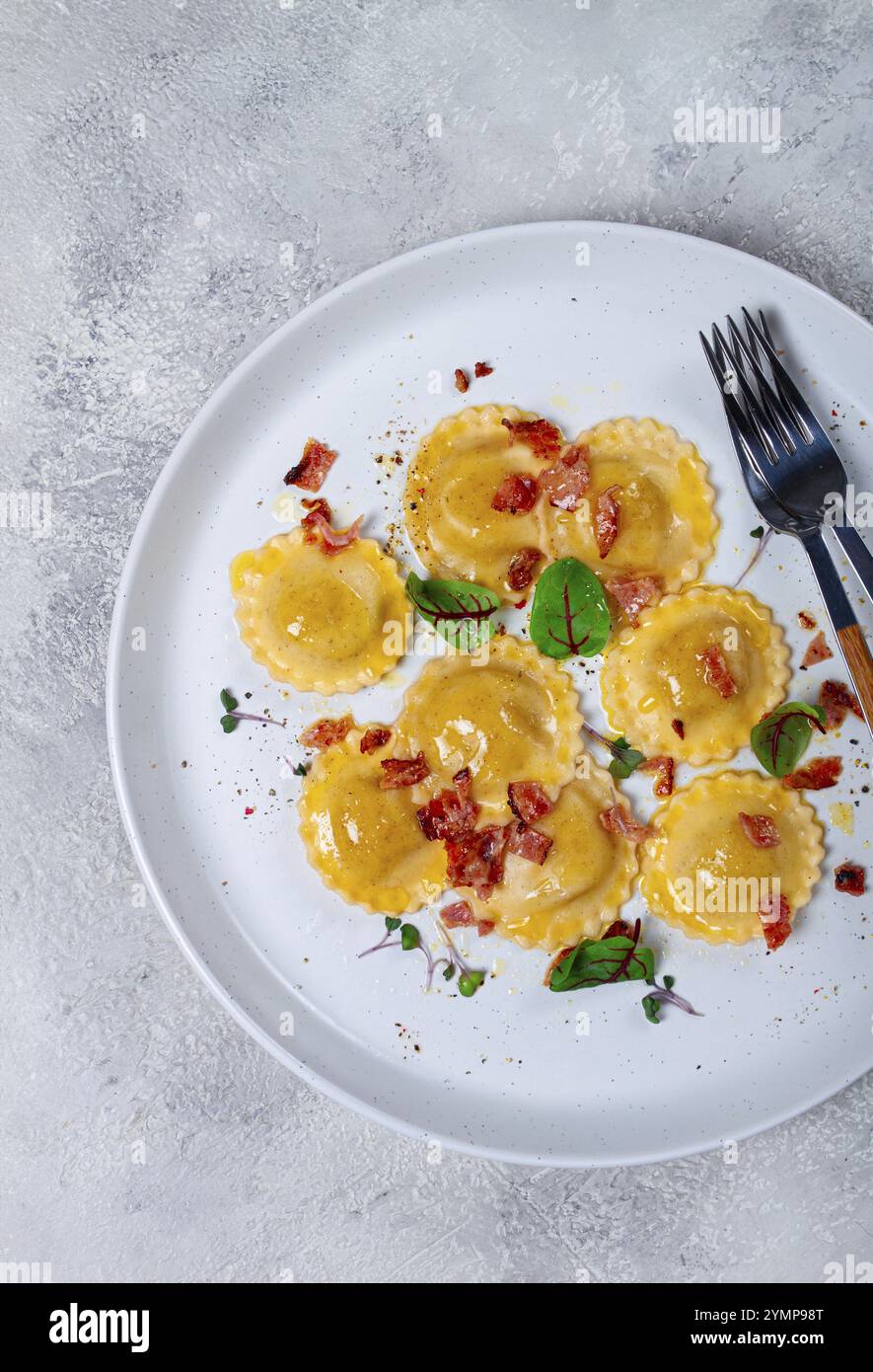 Frische Ravioli, mit Butter, Gewürzen und Kräutern, gebratenem Speck, auf dem Tisch, Draufsicht, heller Hintergrund, keine Leute Stockfoto