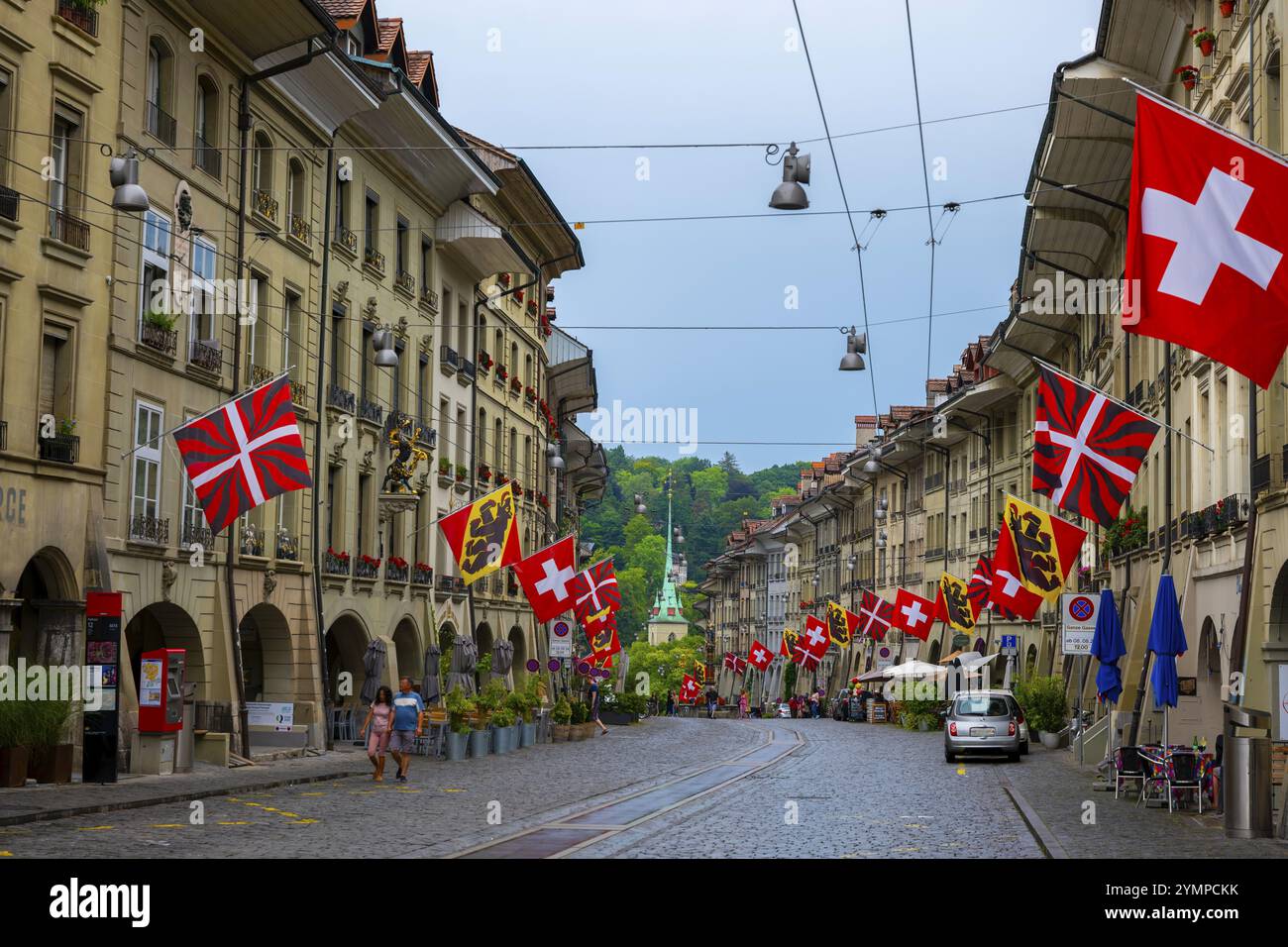 Wunderschöne alte Hauptstraße mit altem Gebäude und Flaggen an einem regnerischen Tag in Bern, Kanton Bern, Schweiz. Stockfoto