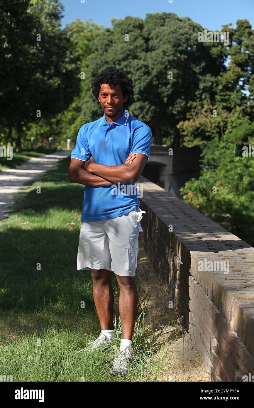 Porträt eines selbstbewussten jungen Athleten, der mit überkreuzten Armen in einem Park steht und eine entspannte und sportliche Einstellung zeigt Stockfoto