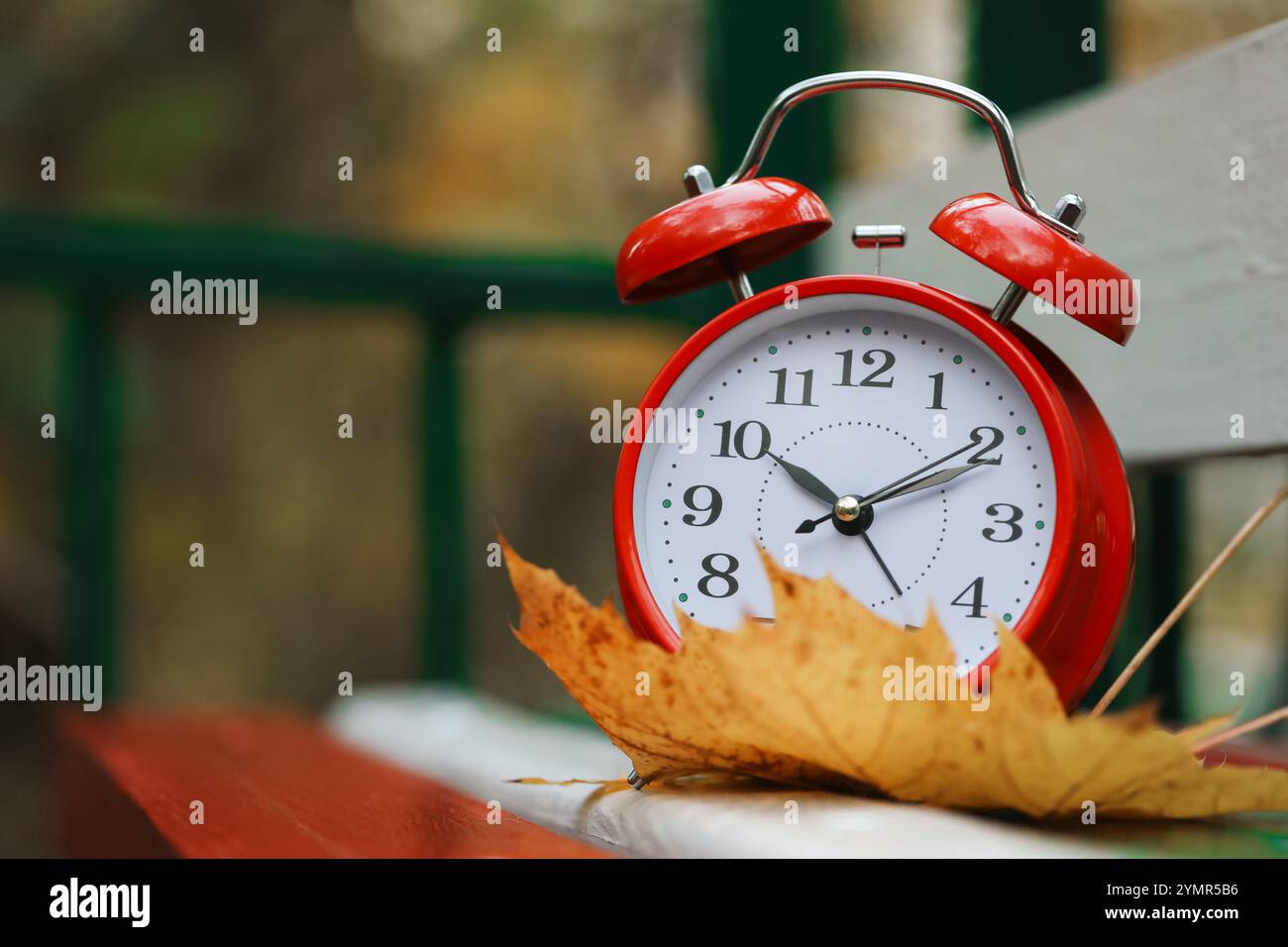 Herbstzeit. Wecker und gefallenes Blatt auf Holzbank im Freien, Platz für Text Stockfoto