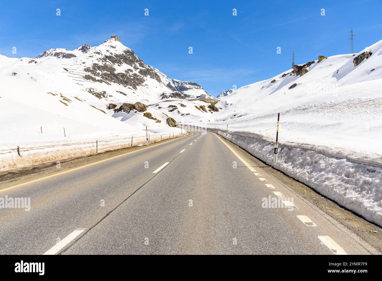 Gewundene Passstraße in einer verschneiten Landschaft in den Schweizer Alpen unter blauem Himmel Stockfoto