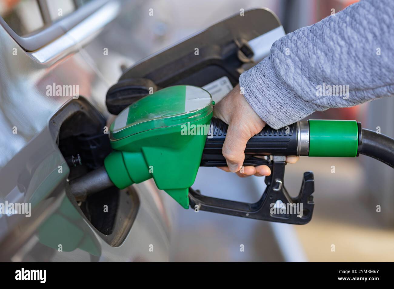 Mann betankt Auto an einer Tankstelle mit grüner Tankdüse an sonnigem Tag. Fahrzeugwartung, Energieressourcen und umweltfreundliche Kraftstofflösungen Stockfoto