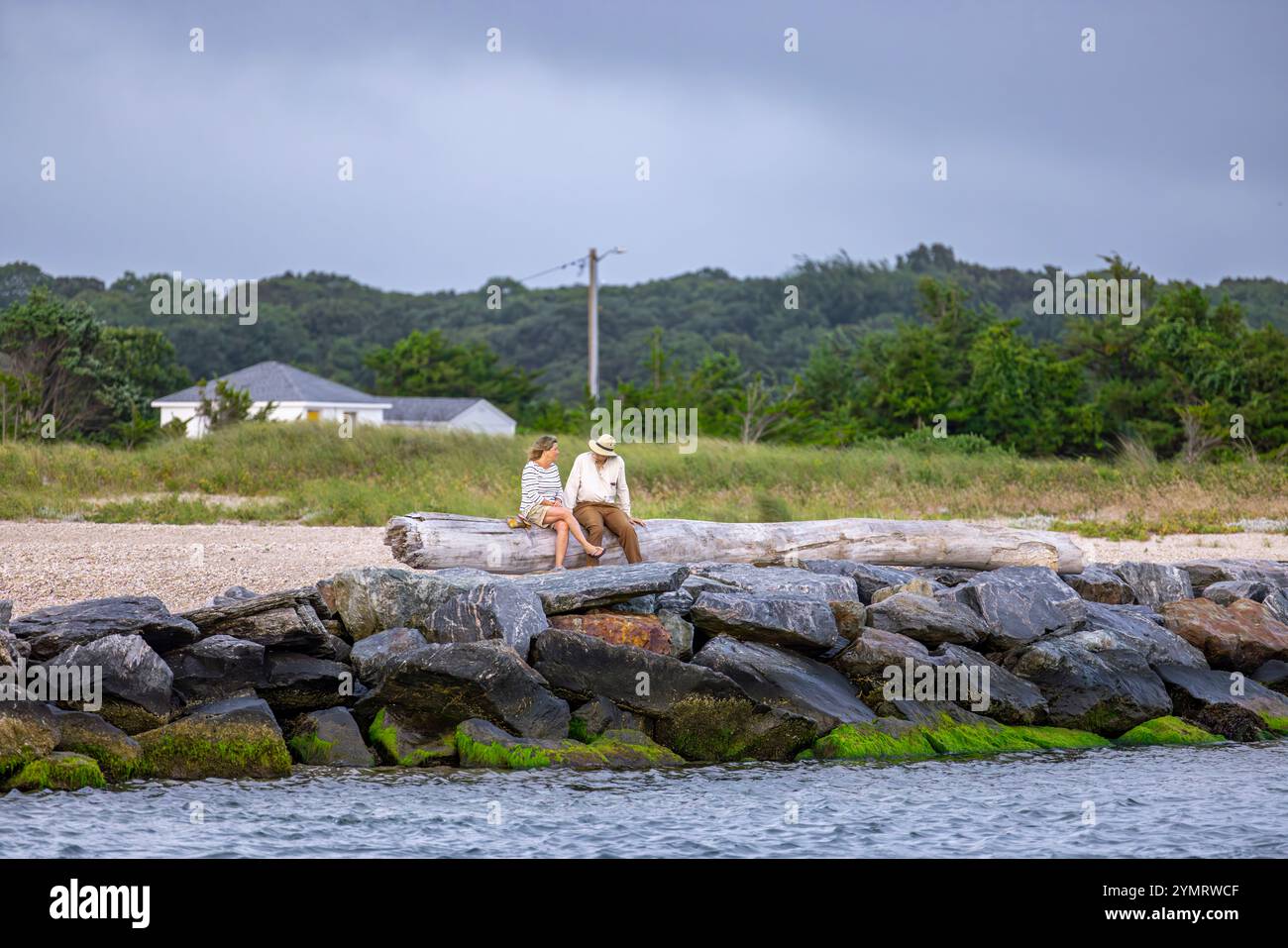 Pärchen, die auf großen Felsen sitzen und am 3-Mile-Hafen reden Stockfoto