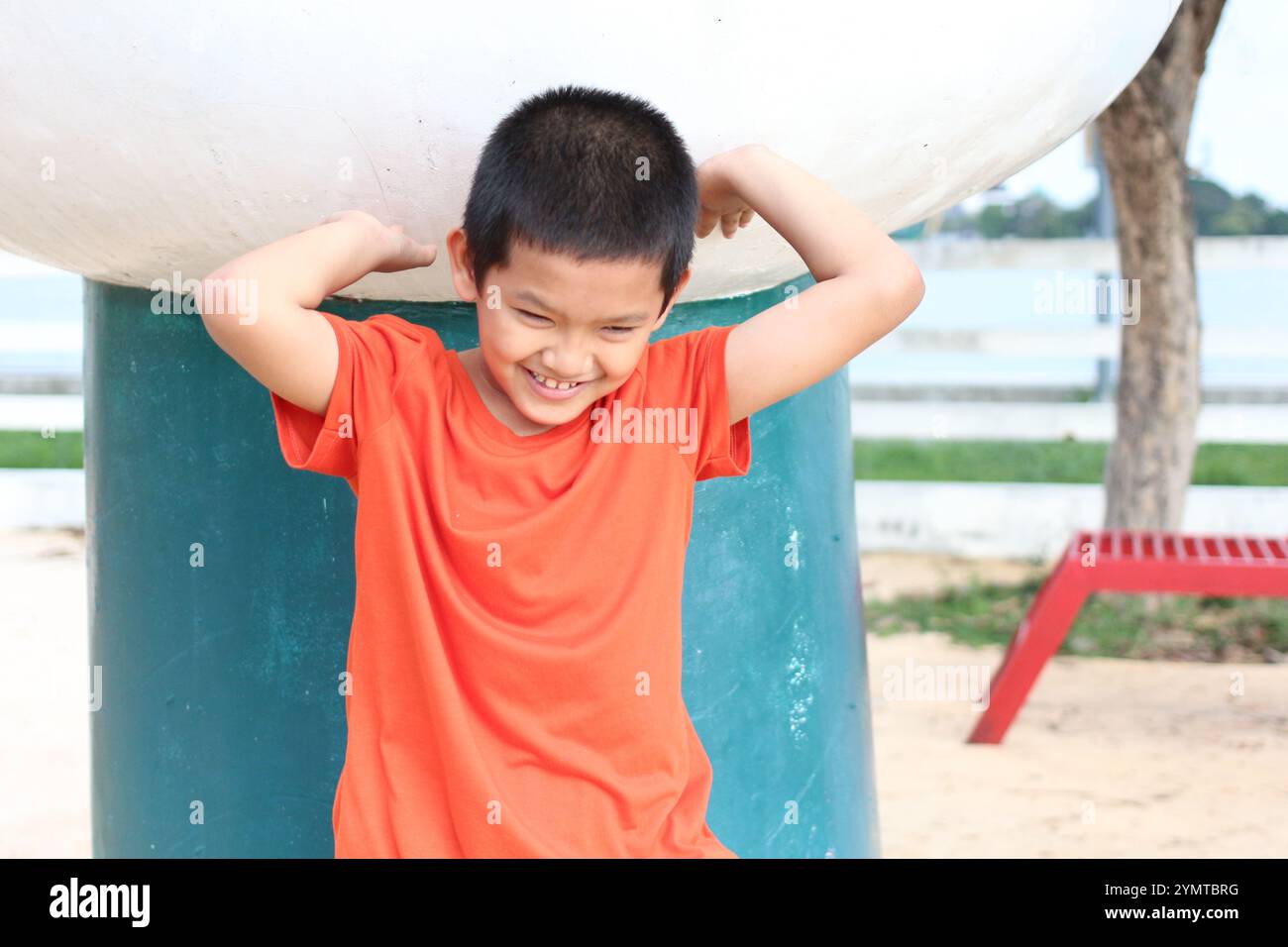 Ein fröhlicher Junge spielt in einem Park im Freien und zeigt Freude und Unschuld. Sein Lächeln spiegelt den unbeschwerten Geist der Kindheit an einem sonnigen Tag wider. Stockfoto