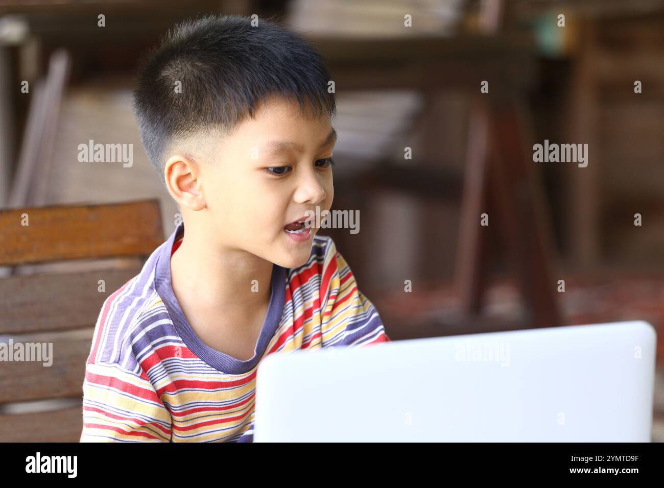 Ein kleiner Junge interagiert mit einem Laptop im Freien und zeigt Neugier und Engagement. Dieses Bild zeigt das Wesen des modernen Lernens und Spielens. Stockfoto