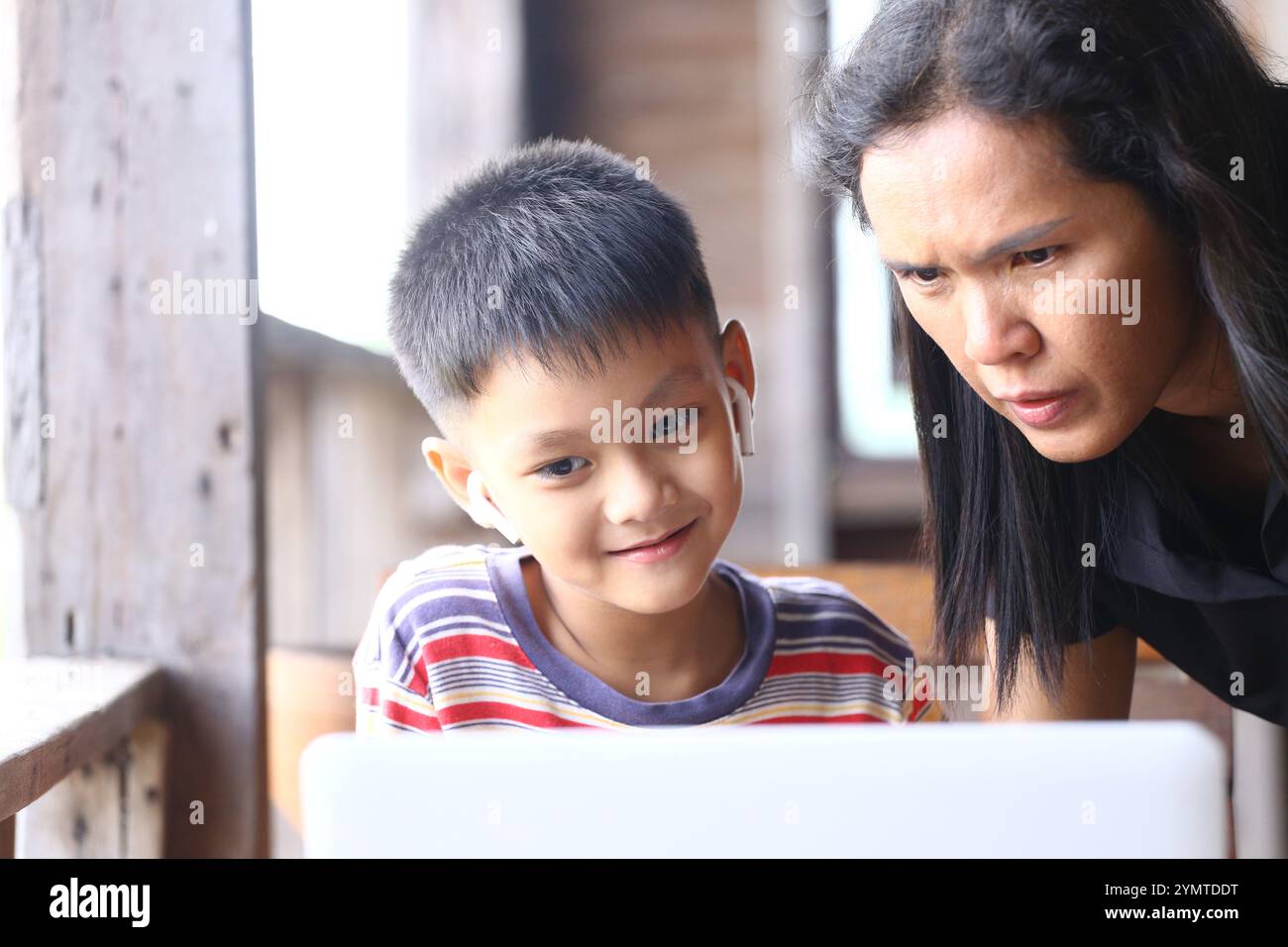 Ein freudiger Moment zeigt, wie ein Kind und ein Elternteil sich mit einem Laptop beschäftigen und wie wichtig die Interaktion mit der Familie bei Lernen und Technologie ist. Stockfoto