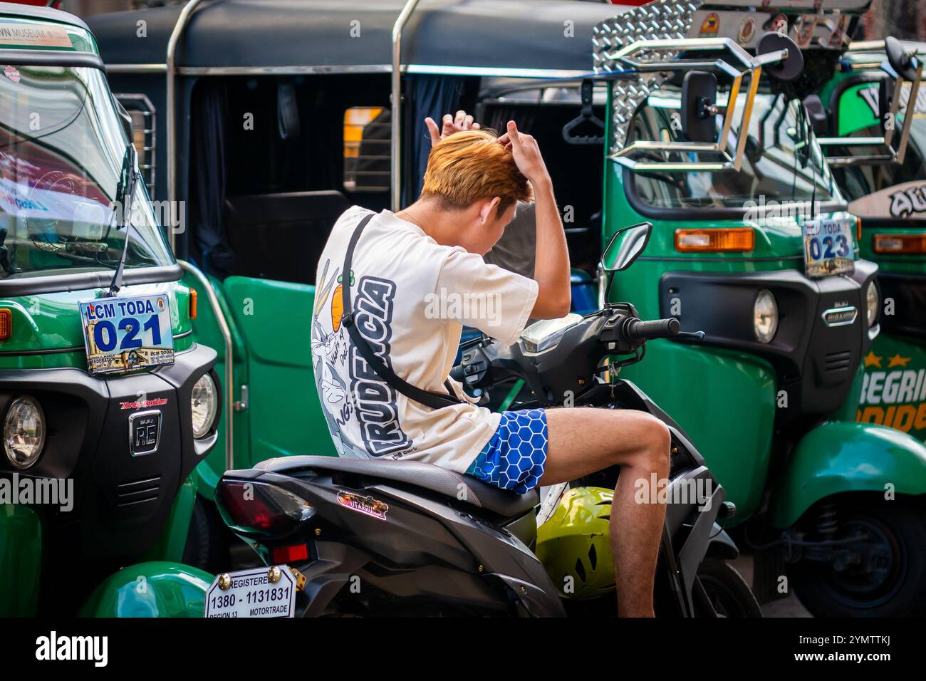 Ein gutaussehender junger philippinischer Junge schaut sich die Haare im Spiegel, der auf seinem Motorrad in der China Town Gegend von Manila auf den Philippinen sitzt. Stockfoto