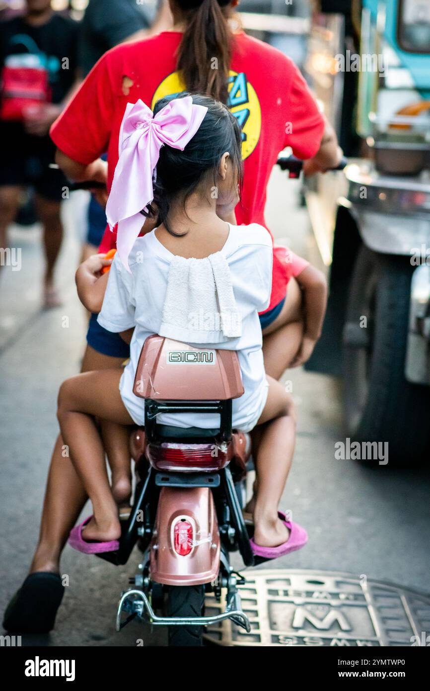 Zwei junge philippinische Kinder saßen auf dem Fahrrad der Mütter und wurden durch die geschäftigen Straßen der China Town Gegend von Manila mitgenommen. Die Philippinen. Stockfoto