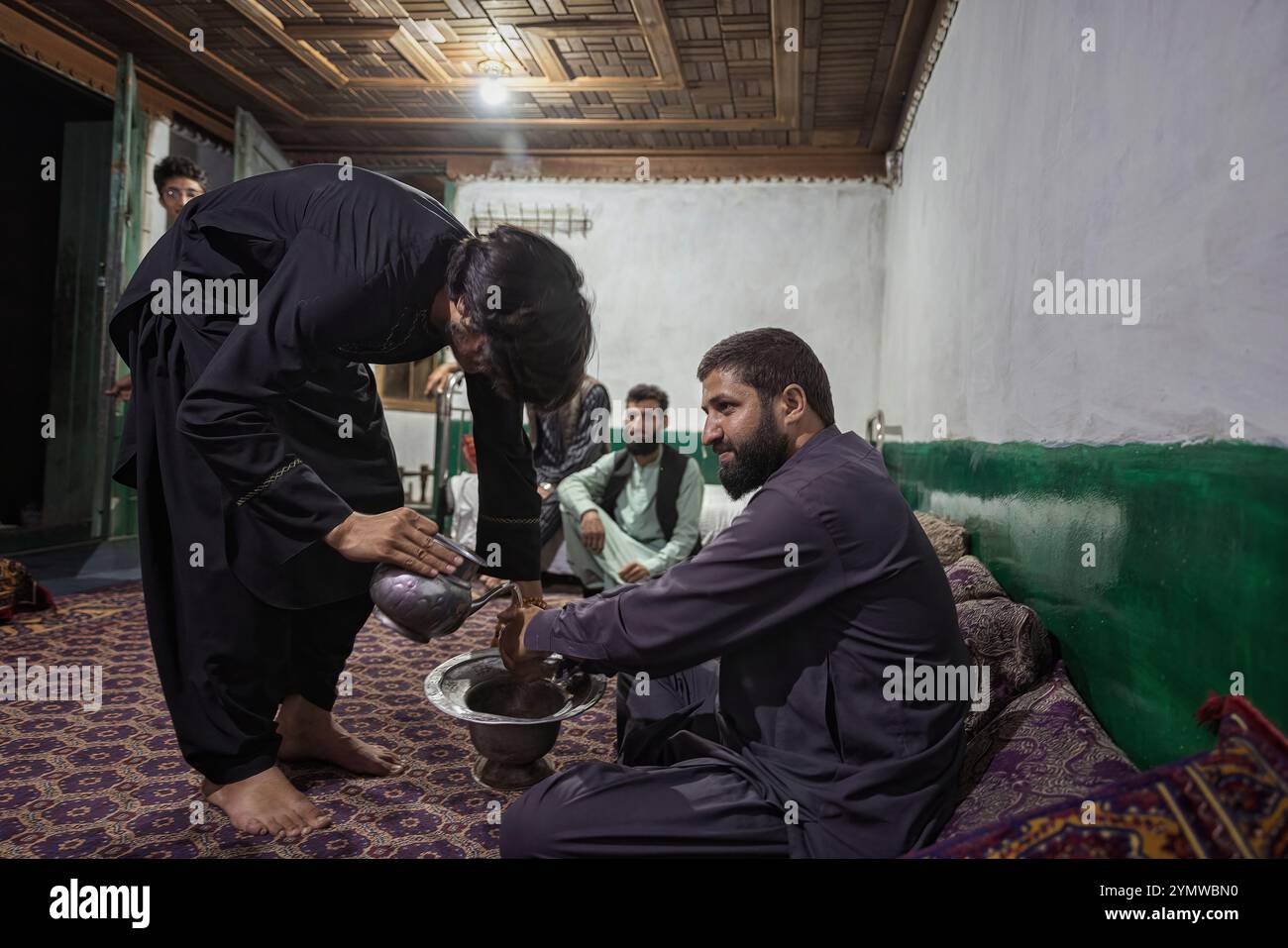 Eine kleine Versammlung in einem Nuristani-Haus. Der Tradition folgend, wäscht der Gastgeber den Gästen vor dem Servieren der Speisen die Hände mit einem traditionellen Pitcher und basi Stockfoto