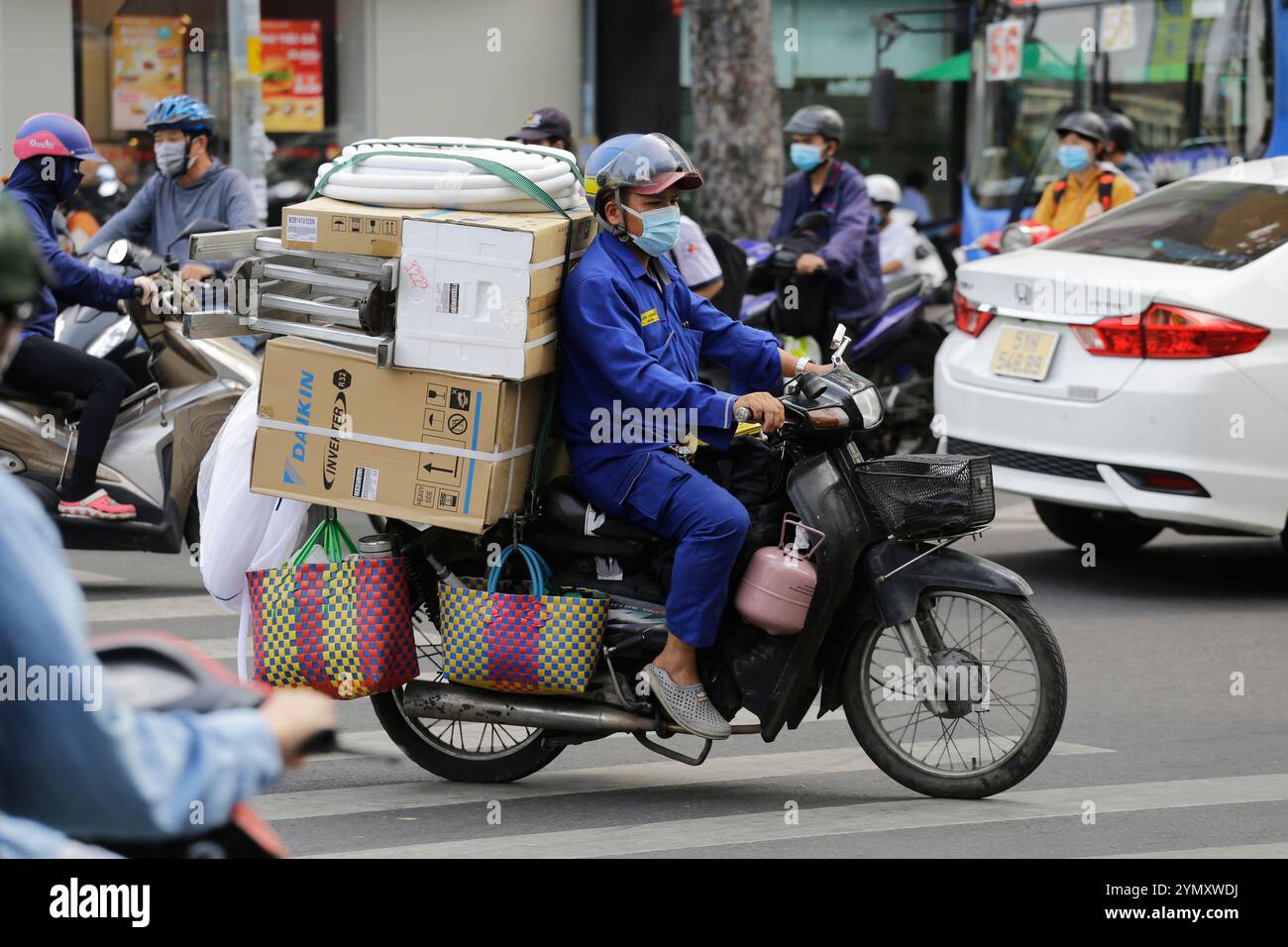 Ho-Chi-Minh-Stadt, Vietnam - 26. Dezember 2022: Ein Motorradfahrer trägt eine Schutzmaske aufgrund schlechter Luftqualität, während er einen überladenen Roller fährt. Stockfoto