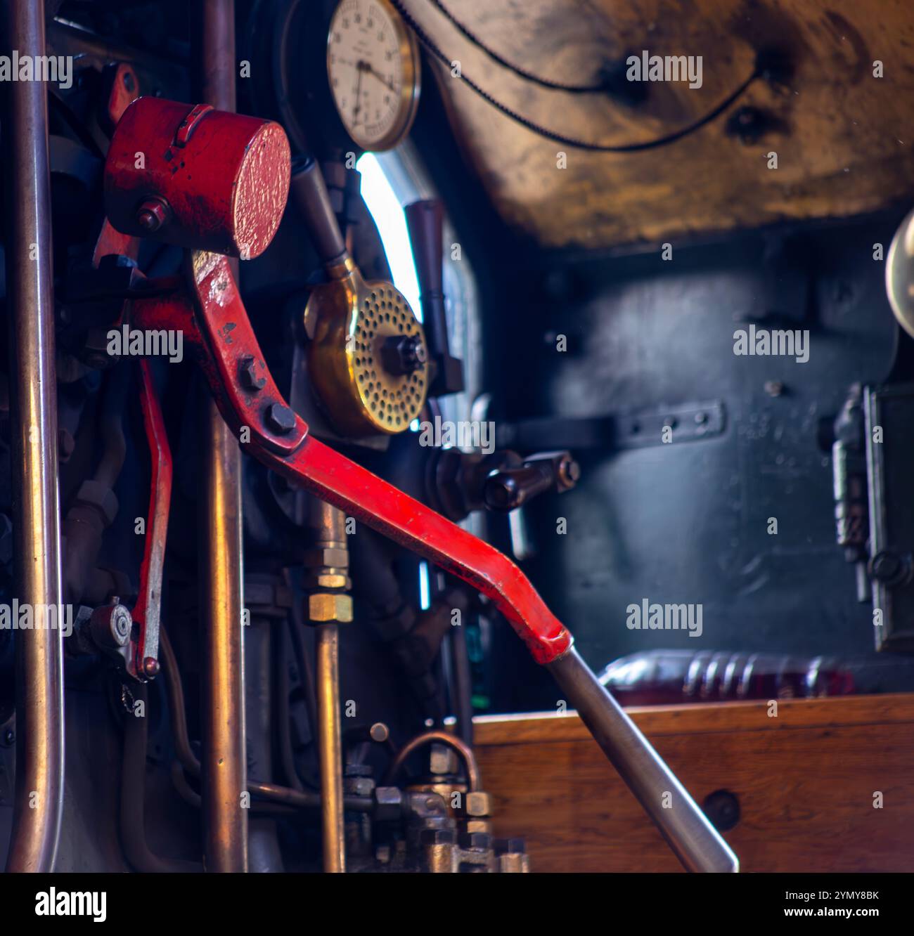 Nahaufnahme des Bedienpults in einer alten Dampflokomotive mit Hebeln, Anzeigen und einem rot lackierten Griff in einer industriellen Umgebung Stockfoto