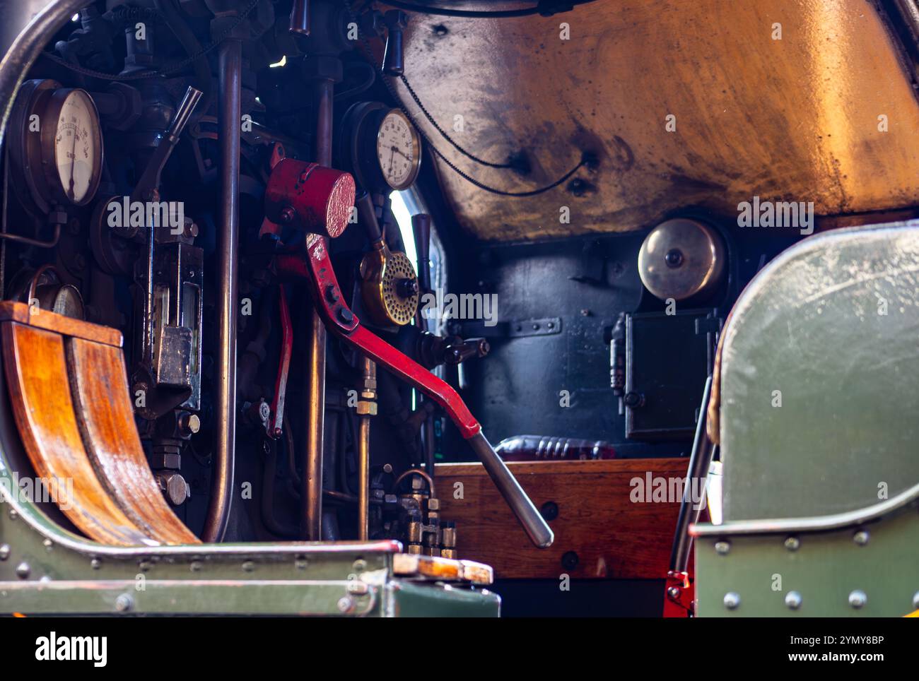 Nahaufnahme des Bedienpults in einer alten Dampflokomotive mit Hebeln, Anzeigen und einem rot lackierten Griff in einer industriellen Umgebung Stockfoto