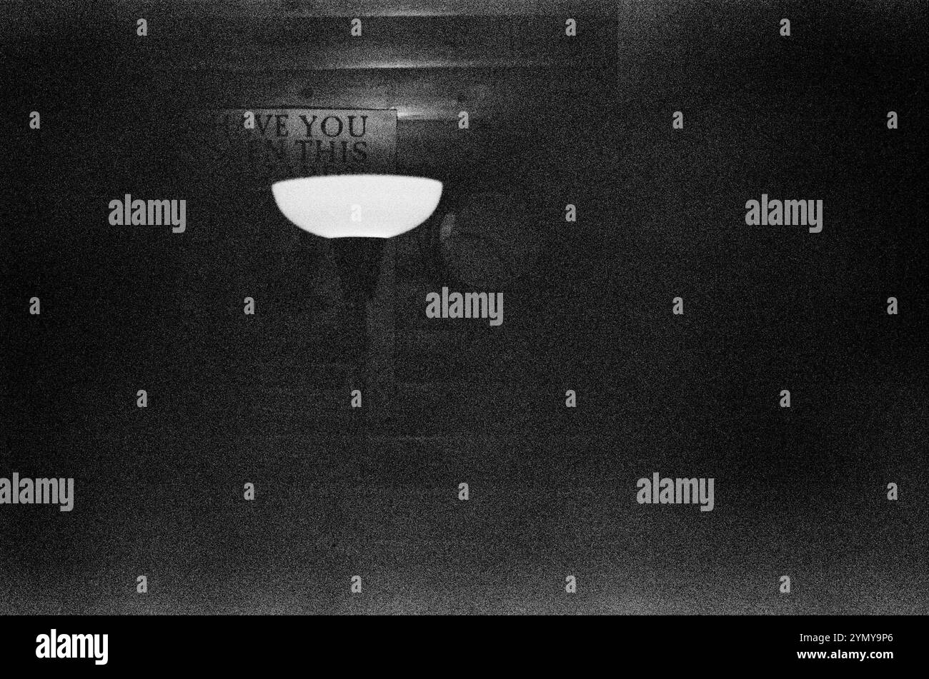 Ein Bild, das ein Schwarzweißfoto einer Lampe in einem schwach beleuchteten Raum zeigt und eine geheimnisvolle und stimmungsvolle Atmosphäre schafft Stockfoto