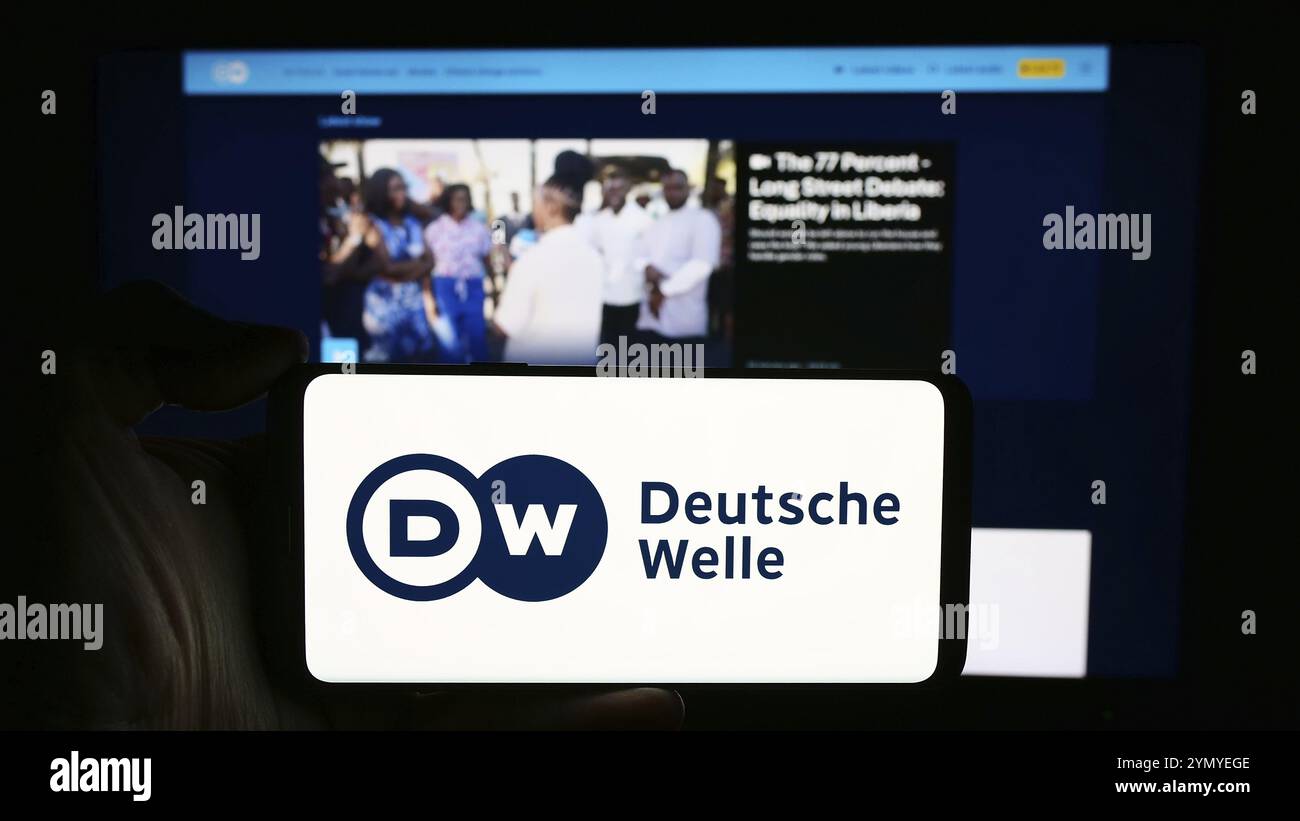 Stuttgart, 10.04.2024: Person mit Handy mit Logo der Deutschen Welle (DW) vor der Webseite. Konzentrieren Sie sich auf Stockfoto
