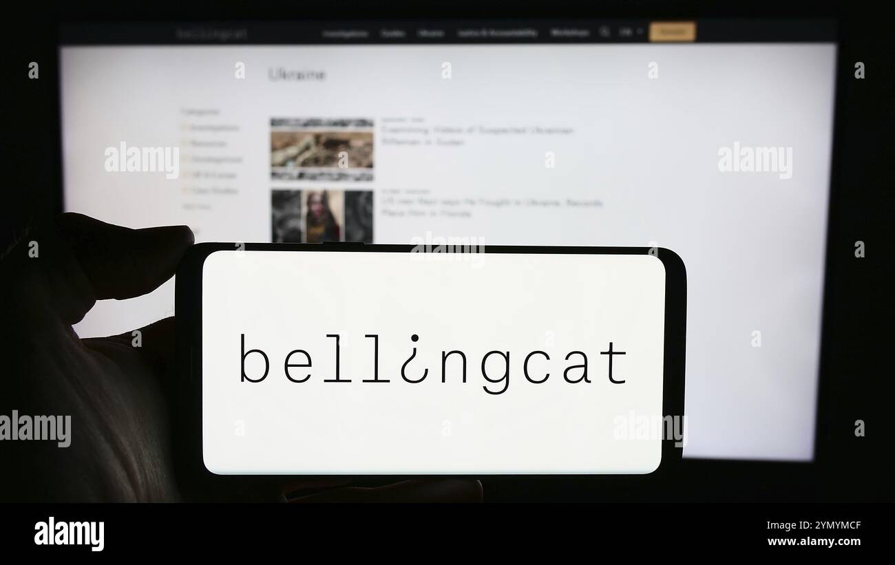 Stuttgart, Deutschland, 03.06.2024: Person mit Handy mit Logo der niederländischen investigativen Journalismusorganisation Bellingcat vor der Webseite. Fokussieren Stockfoto
