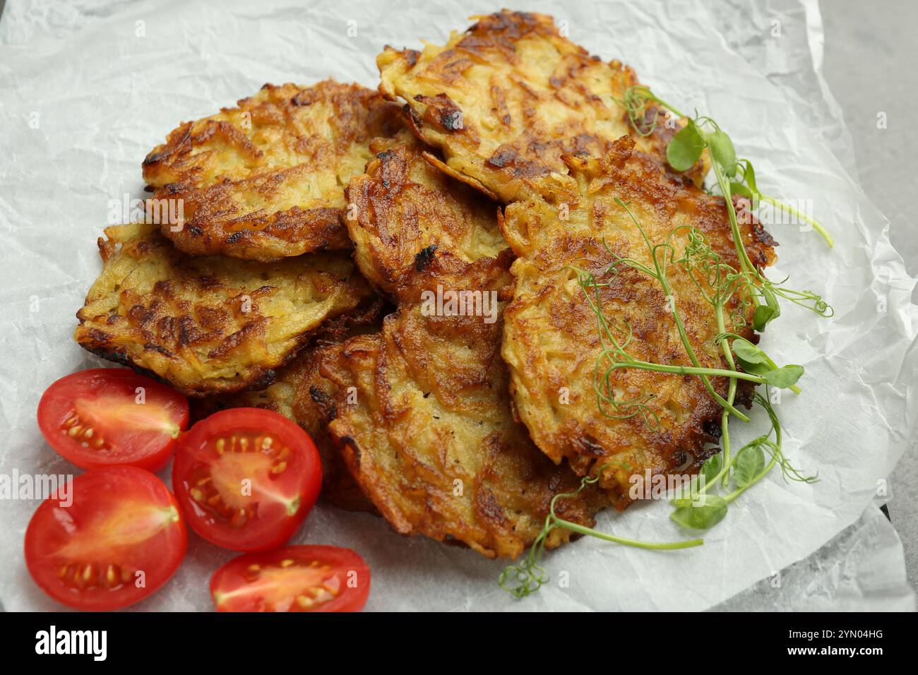 Köstliche Kartoffelpfannkuchen mit frischen Tomaten und Mikrogrün auf dem Tisch, Nahaufnahme Stockfoto
