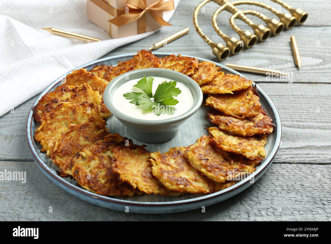 Leckere Kartoffelpfannkuchen, Menora und Geschenkbox auf grauem Holztisch, Nahaufnahme. Hanukkah festliches Essen Stockfoto