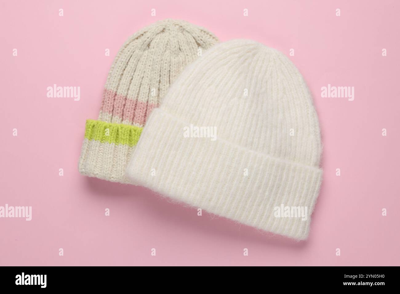 Warme Wollmützen auf hellrosa Hintergrund, Draufsicht Stockfoto