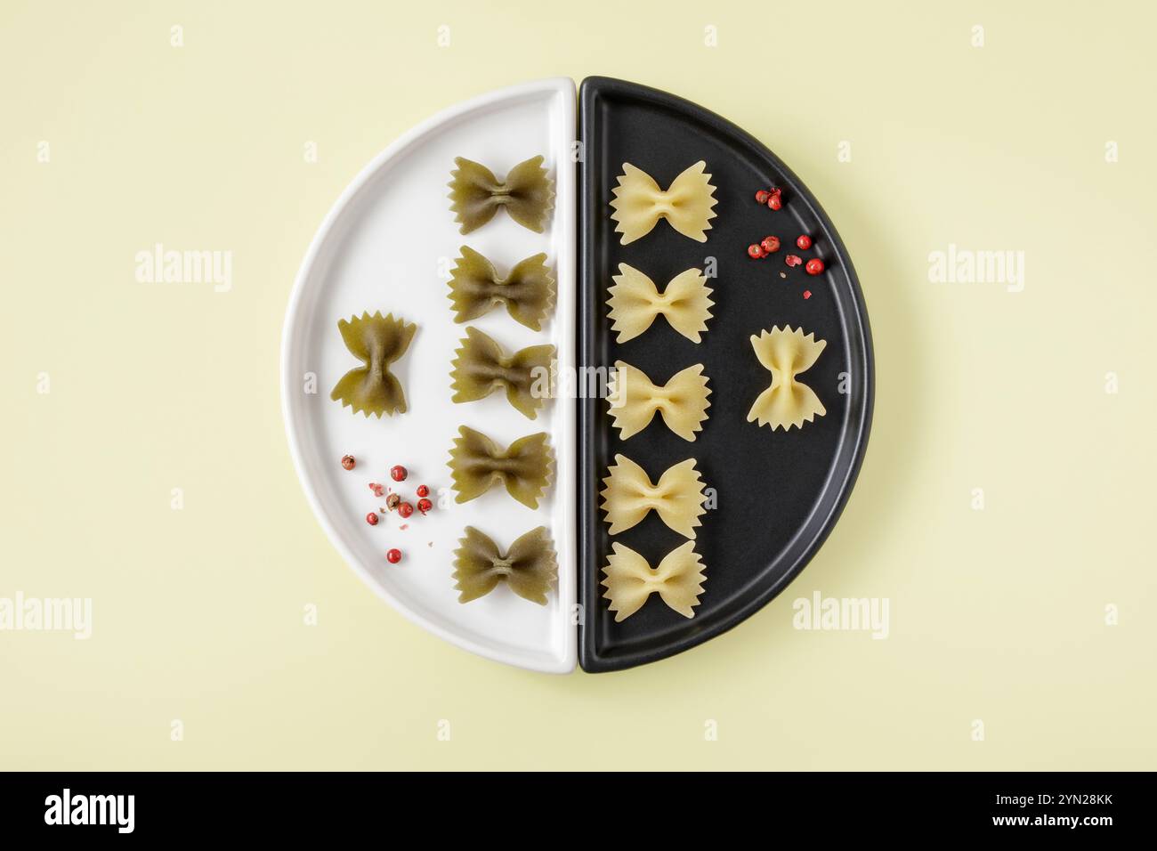 Kleine Farfalle Pasta auf schwarz-weißem Teller mit roten Pfefferkörnern Stockfoto