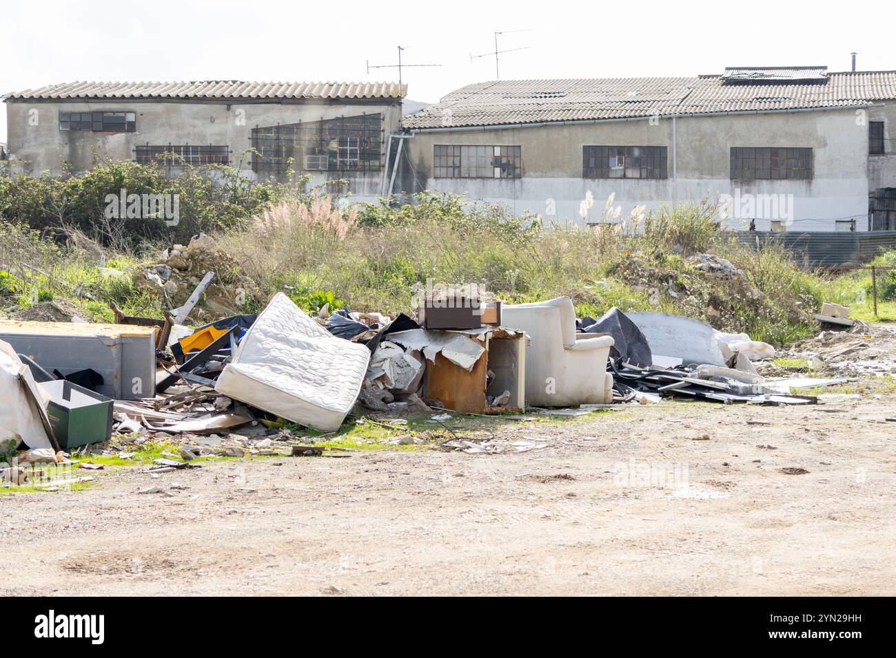 Fliegen, das die Umwelt mit alten Möbeln, Matratzen und anderen Haushaltsabfällen in der Nähe einer stillgelegten Fabrik verschmutzt Stockfoto