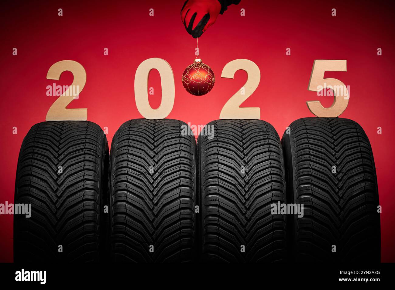 Winterreifen und Mechaniker in roten Handschuhen halten weihnachtsbaumkugel, 2025 Happy New Year Hintergrund Stockfoto