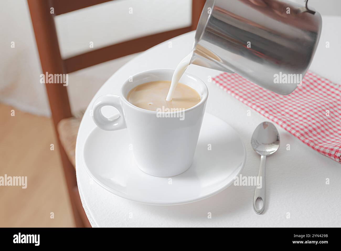 Kaffee mit Milch in einer weißen Tasse auf einer Untertasse auf einem weißen Holztisch. Stockfoto