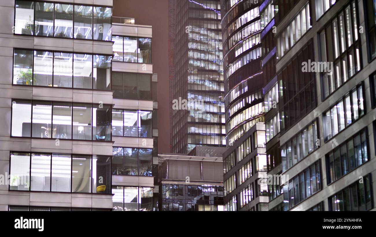 Bürogebäude am Abend mit beleuchteten Arbeitsplätzen. Moderner, verglaster Wolkenkratzer im Finanzviertel. Späte Öffnungszeiten im Büro. Stockfoto