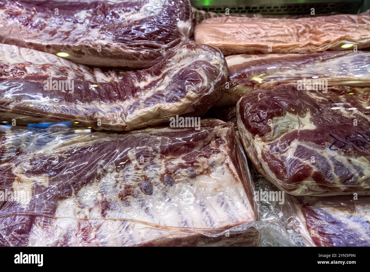 Große Stücke von rohem gekühltem Fleisch vakuumverpackt in einer Metzgerei Vitrine. Stockfoto