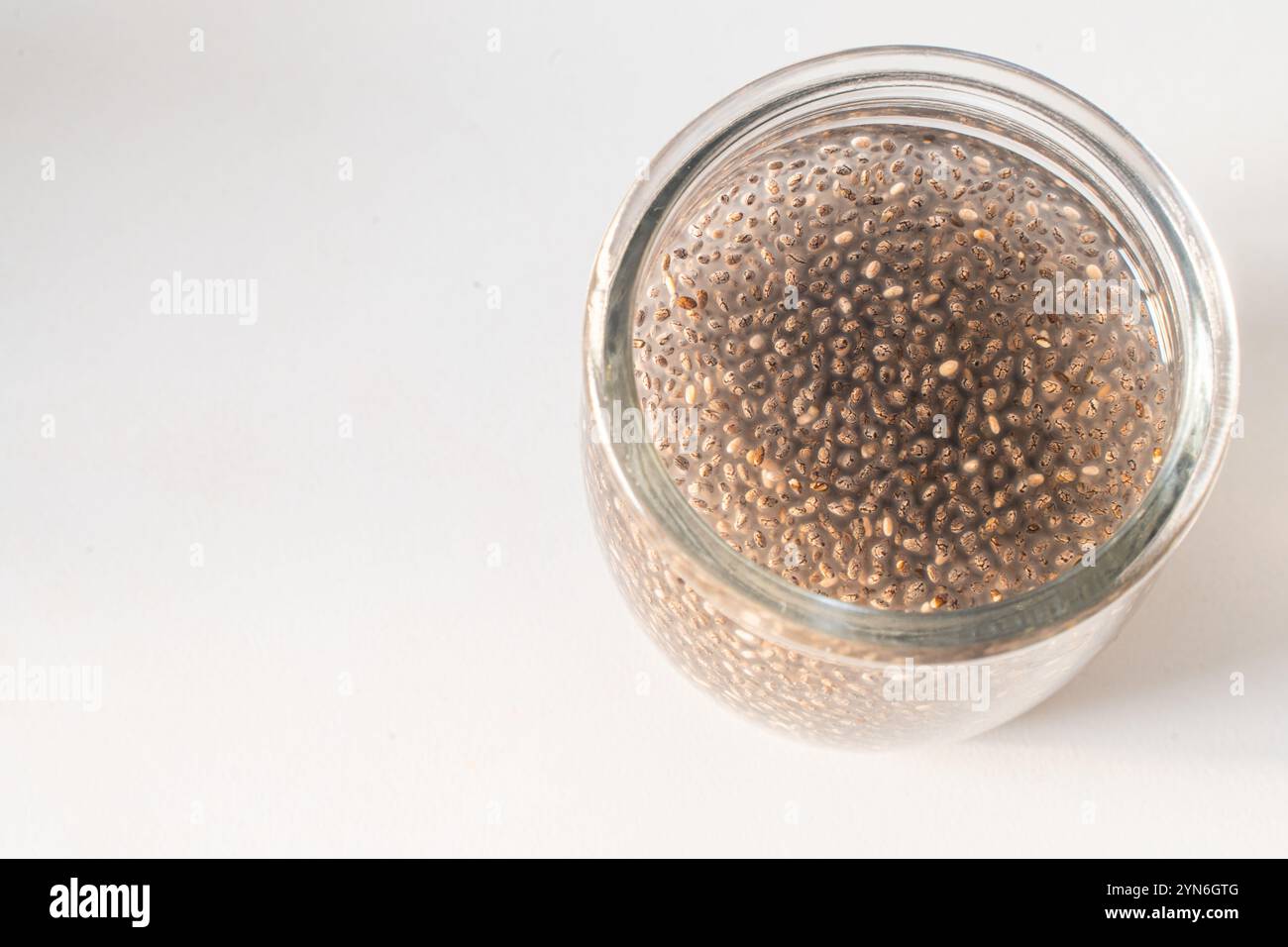 Chiasamen in Wasser in einem Glas auf einem weißen Tisch eingeweicht. Das Konzept der gesunden, diätetischen Ernährung. Hochwertige Fotos Stockfoto