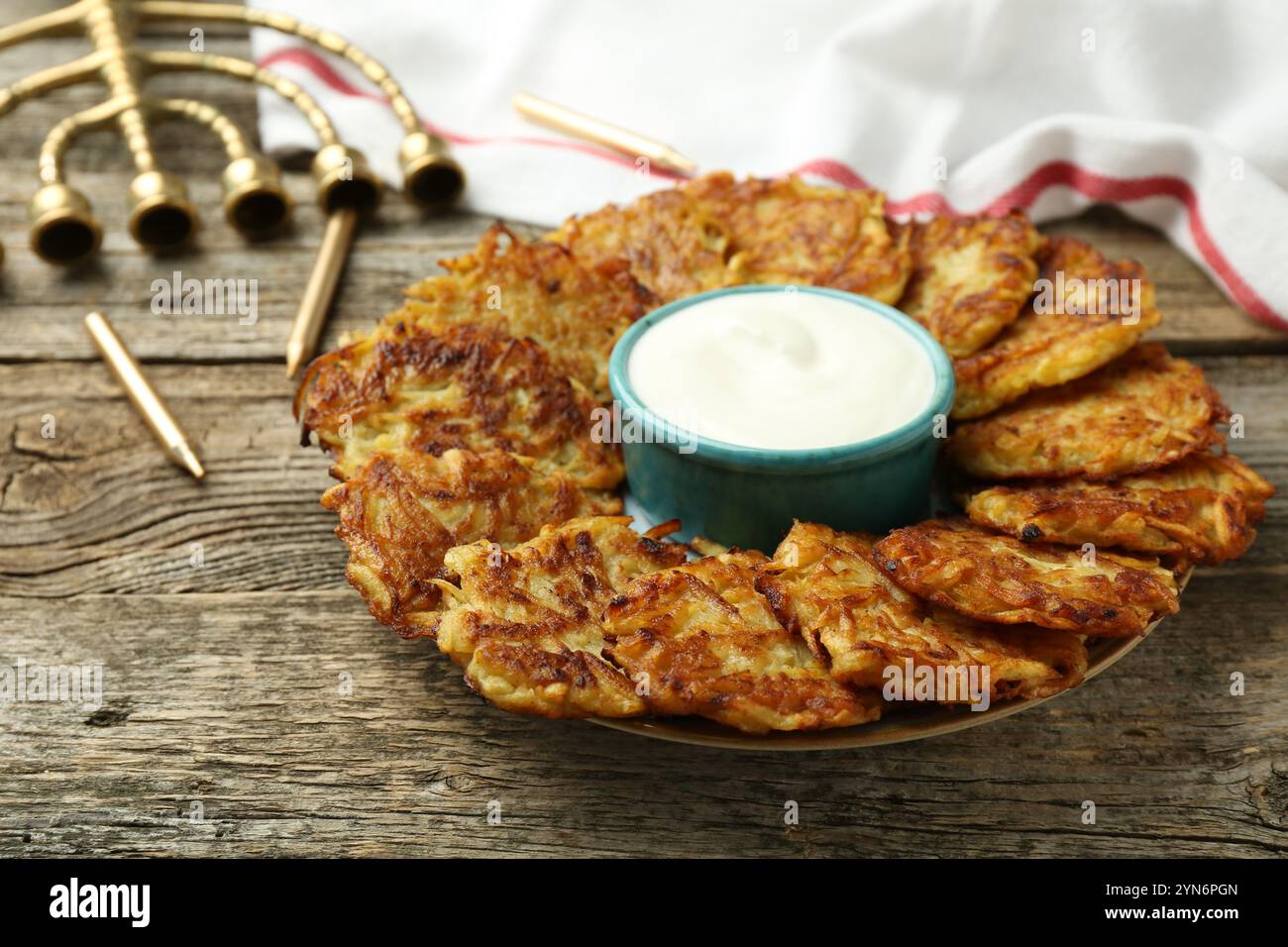 Leckere Kartoffelpfannkuchen, Sauerrahm, Menora und Kerzen auf Holztisch, Nahaufnahme. Hanukkah festliches Essen Stockfoto