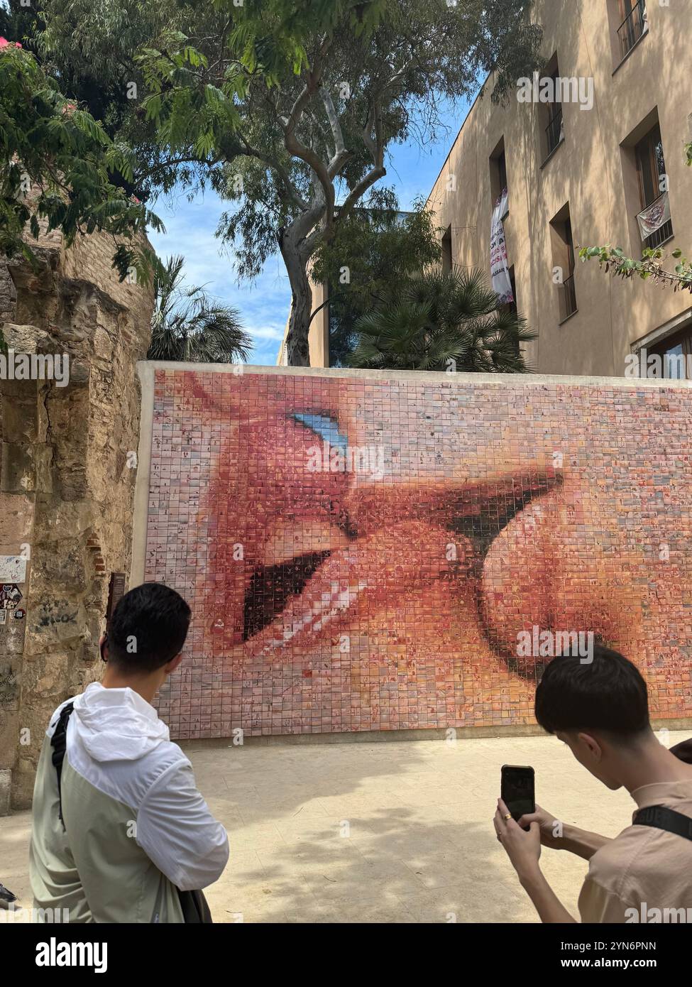 Asiatische Touristen sehen und fotografieren den „Kuss der Freiheit“ in Barcelona, Spanien - Smartphone-aufgenommenes Stockfoto