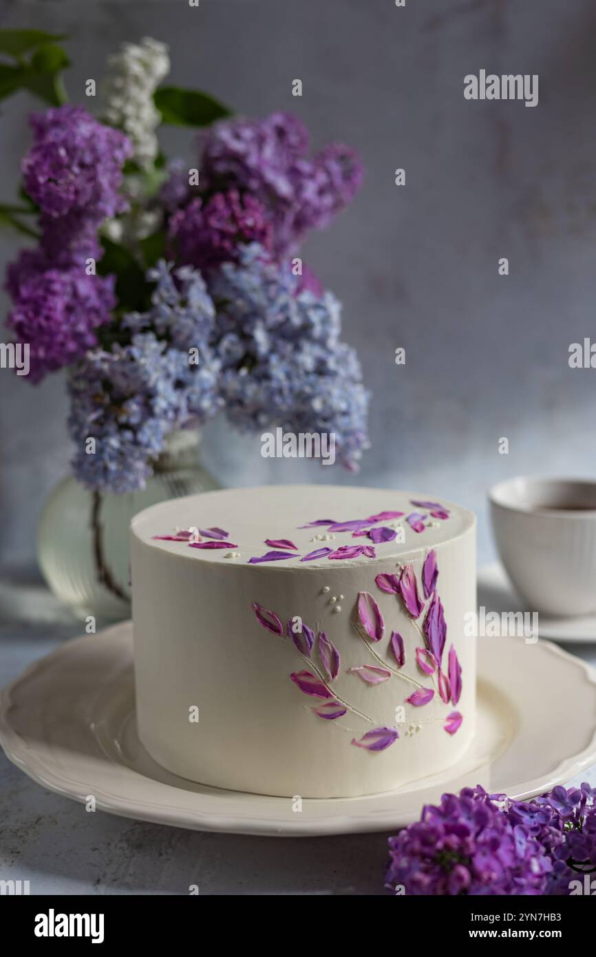 Eleganter Kuchen mit floralem Buttercremedekor und Fliederstrauß in weichem Tageslicht, perfekt für Feiern und künstlerische Fotografie-Konzepte Stockfoto