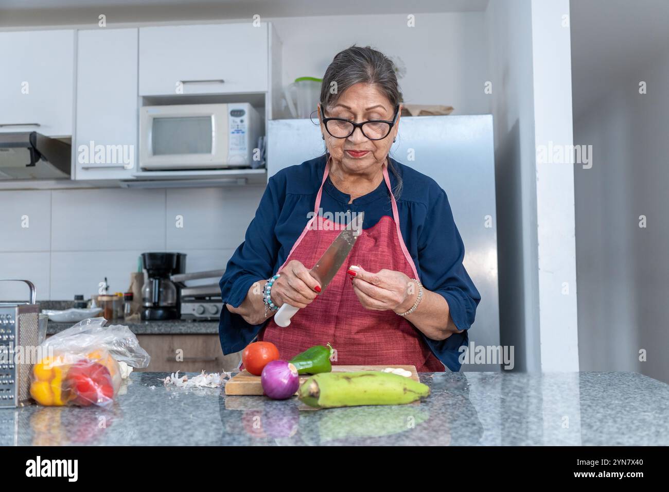 Eine Frau schneidet Gemüse auf einer Theke. Sie trägt eine rote Schürze und hat ein Messer in der Hand Stockfoto