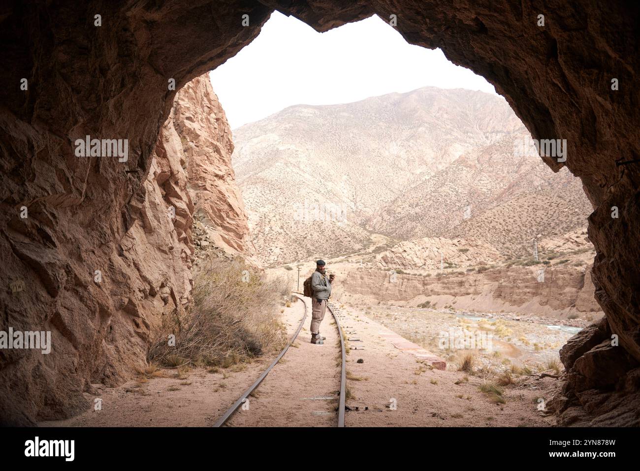 Ausgang eines Zugtunnels, draußen sieht ein Mann lächelnd in die Kamera. Im Hintergrund eine Andenlandschaft. Stockfoto