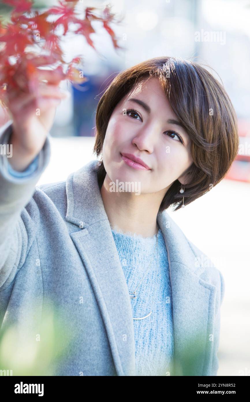 Lächelnde Frau in ihren 30ern, die Herbstblätter berührt Stockfoto