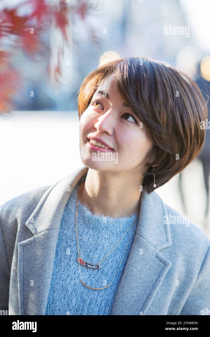 Lächelnde Frau in ihren 30ern, die die Herbstblätter genießt. Stockfoto