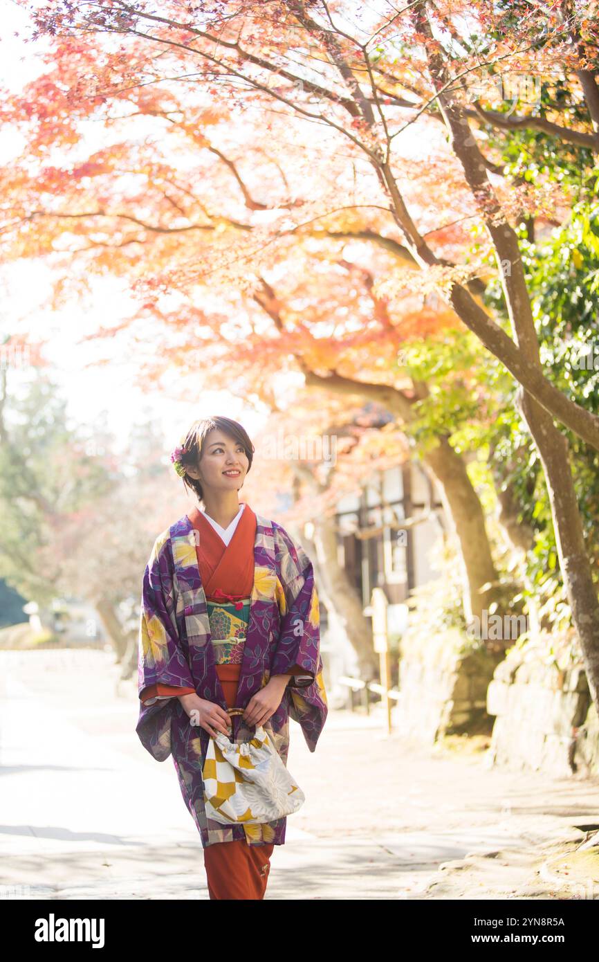 Lächelnde Frau in ihren 30ern, die auf Herbstlaub blickt. Stockfoto