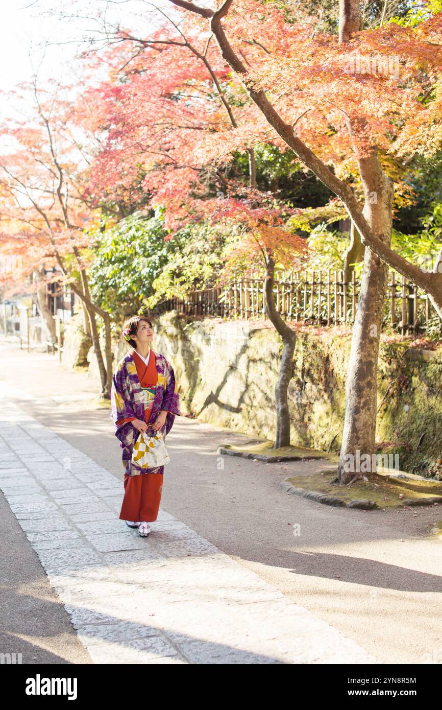 Lächelnde Frau in ihren 30ern, die auf Herbstlaub blickt. Stockfoto