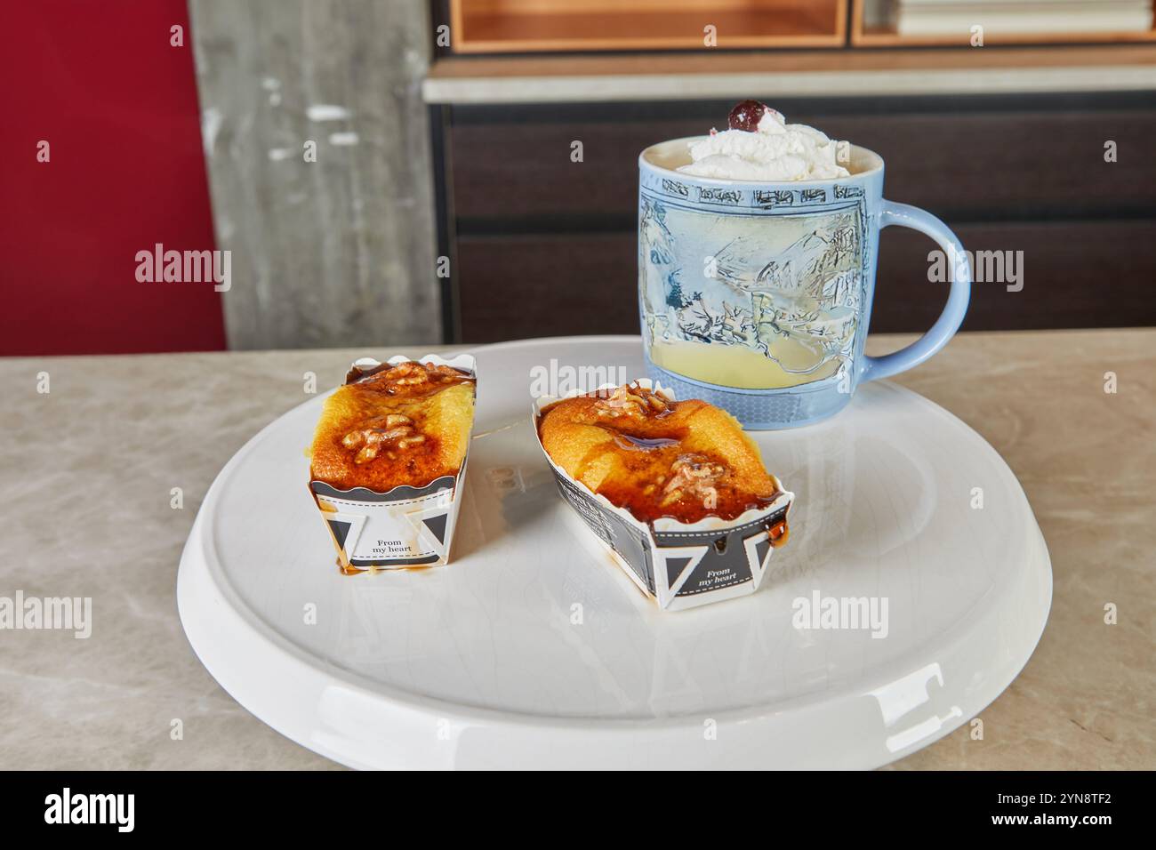 Goldene Walnussmuffins, serviert zusammen mit einem Schlagsahne Latte in einer gemütlichen Küche, perfekt für einen süßen Genuss. Stockfoto