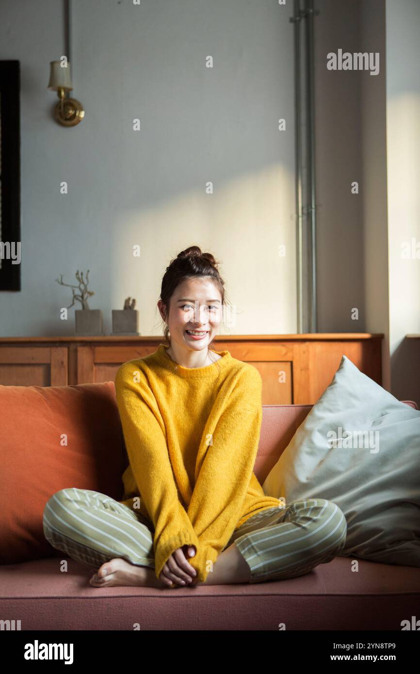Lächelnde Frau in ihren 20ern, die im Kreuz auf einem Sofa sitzt Stockfoto