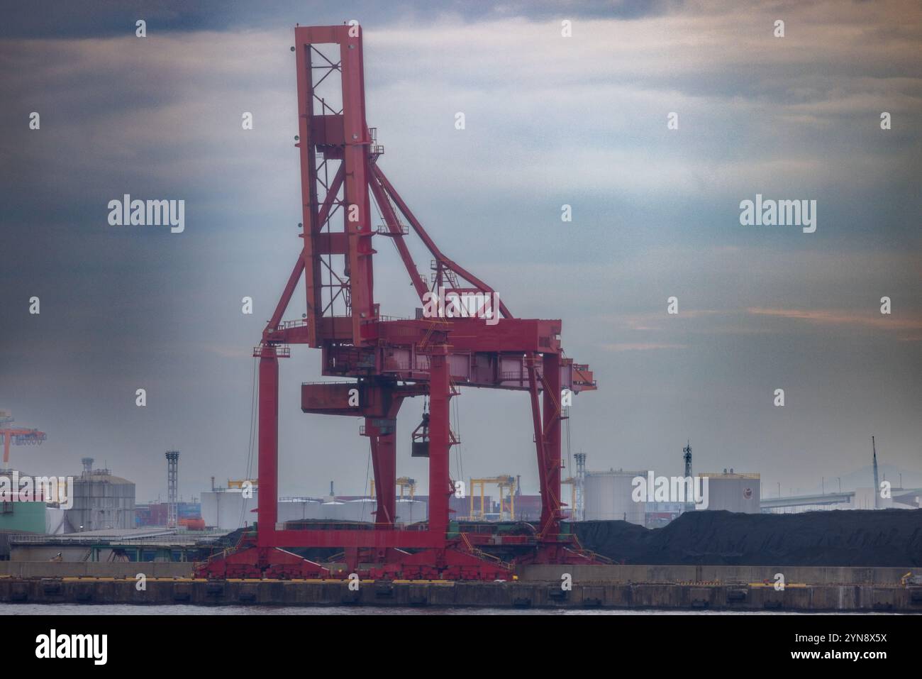 Roter Industriekran gegen eine bewölkte Skyline im Hafen Stockfoto