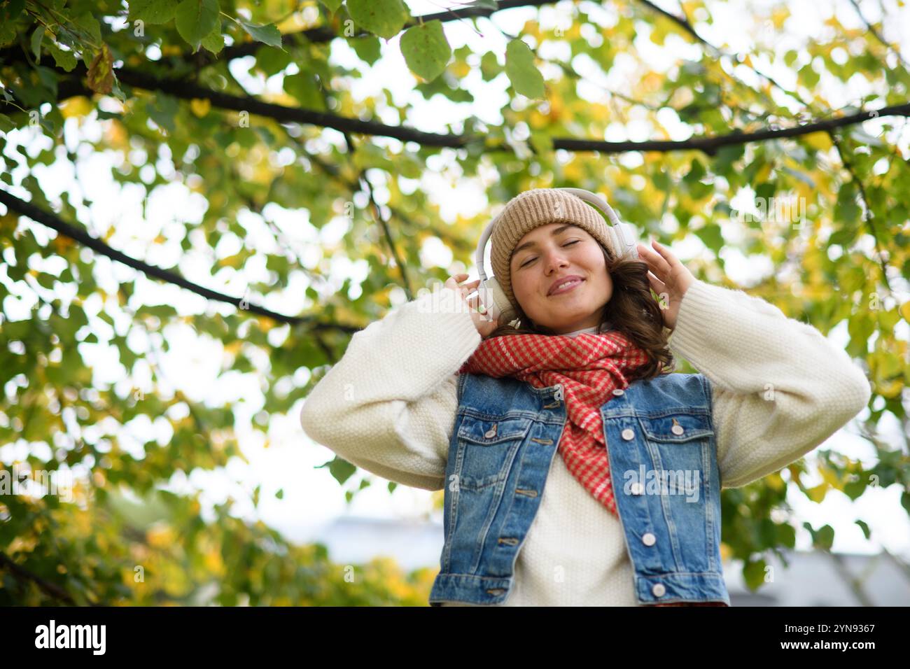 Schöne junge Frau, die im Herbstpark spaziert, Musik hört und einen friedlichen Moment für sich selbst genießt. Stockfoto