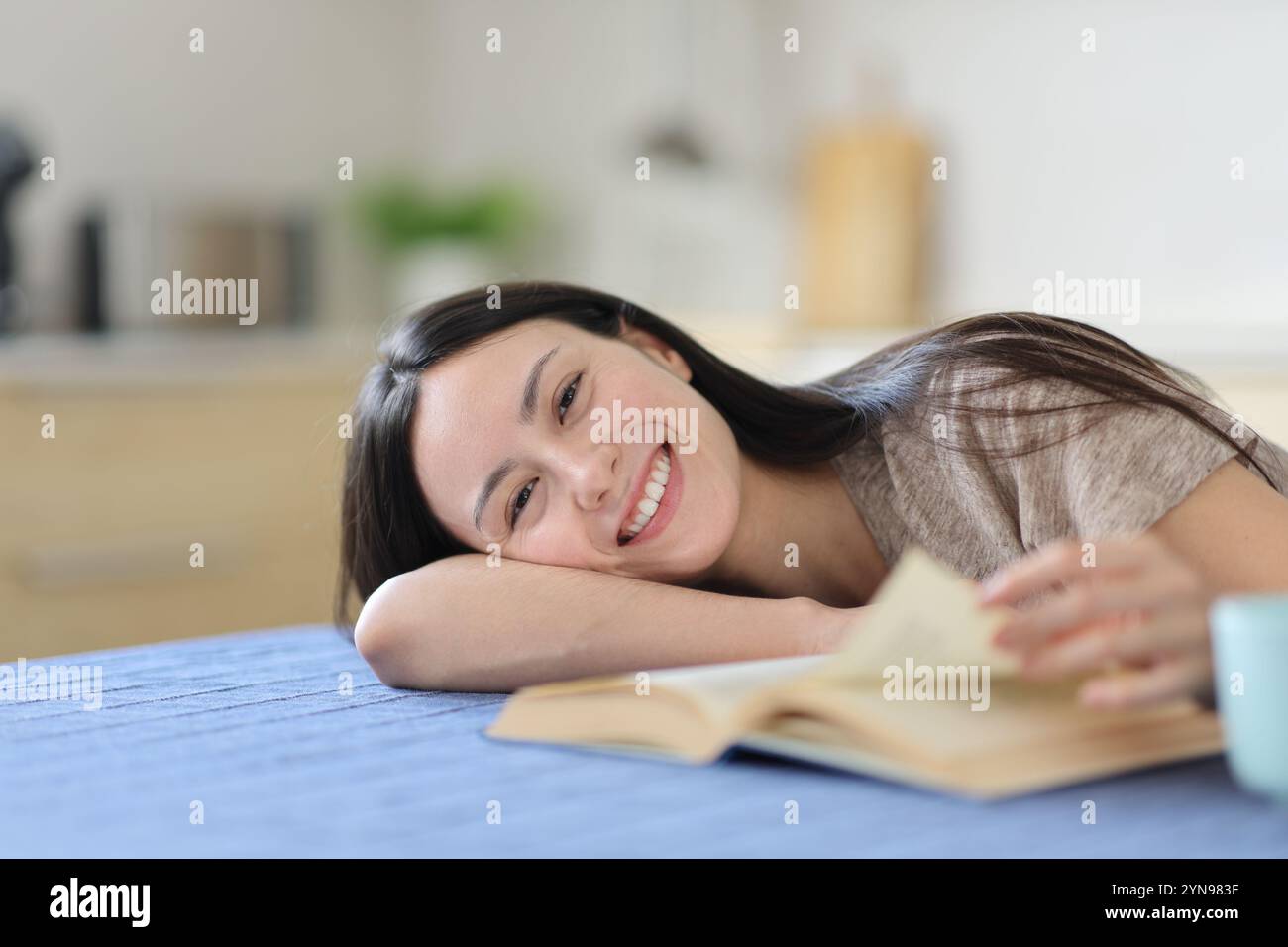 Asiatische Frau, die ein Buch liest, sieht dich in der Küche zu Hause an Stockfoto