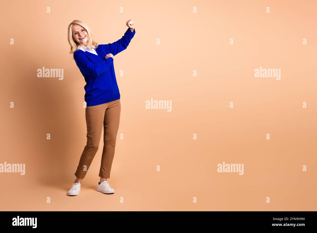 Elegante ältere Frau im blauen Pullover lächelt vor beigefarbenem Hintergrund Stockfoto