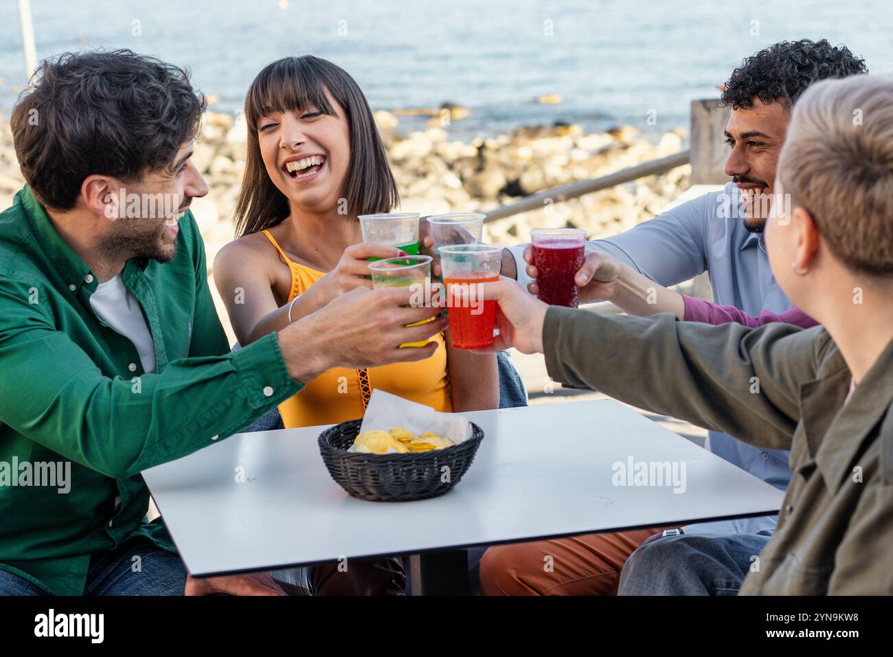 Ehrlicher Moment junger multikultureller Freunde, die mit Getränken in der Strandbar feiern. Natürliche Ausdrucksformen von Freude und Lachen während des Sommergeselliges Stockfoto