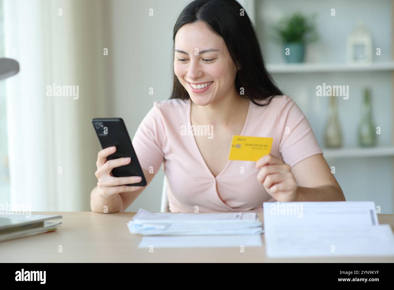 Glückliche asiatische Frau, die Rechnungen online mit Kreditkarte und Telefon zu Hause bezahlt Stockfoto