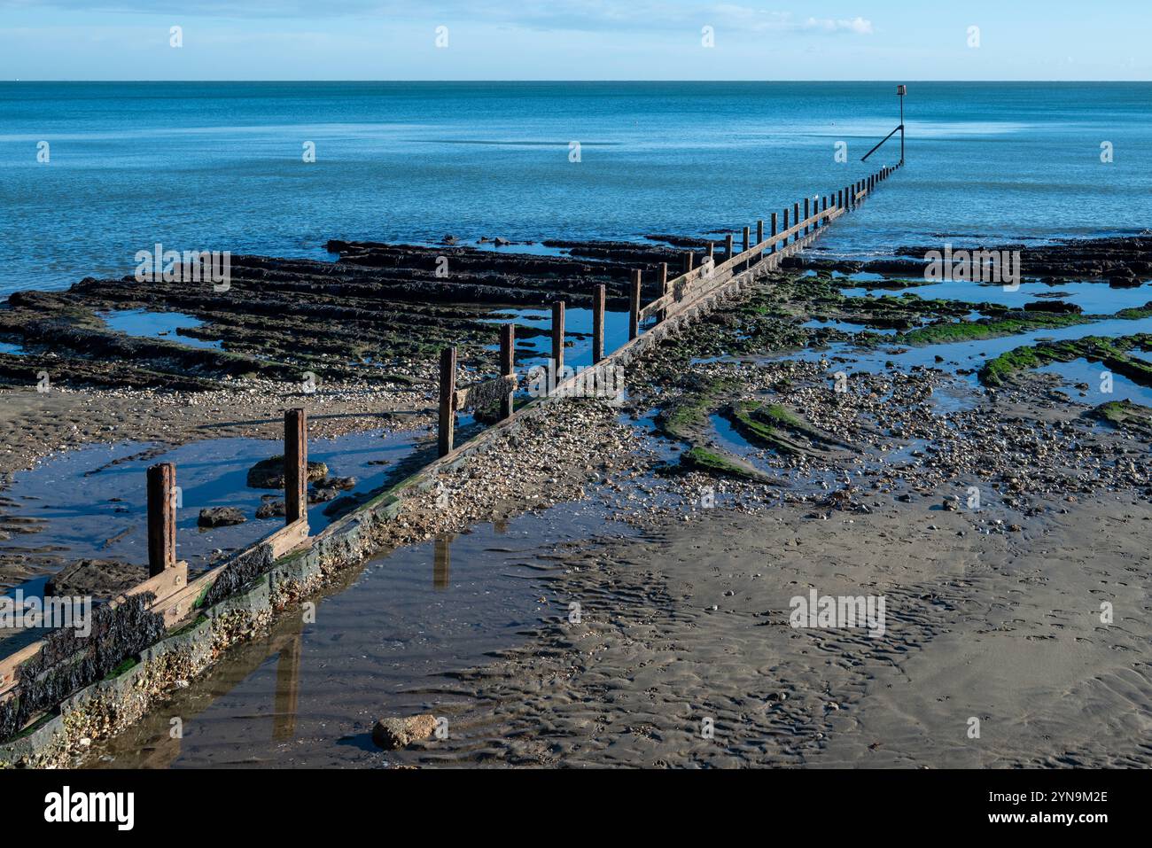 Wellenbrecher bei Ebbe an einem Sandstrand in England, mit ruhigem, blauem Wasser und niemandem dabei. November 2024. Stockfoto