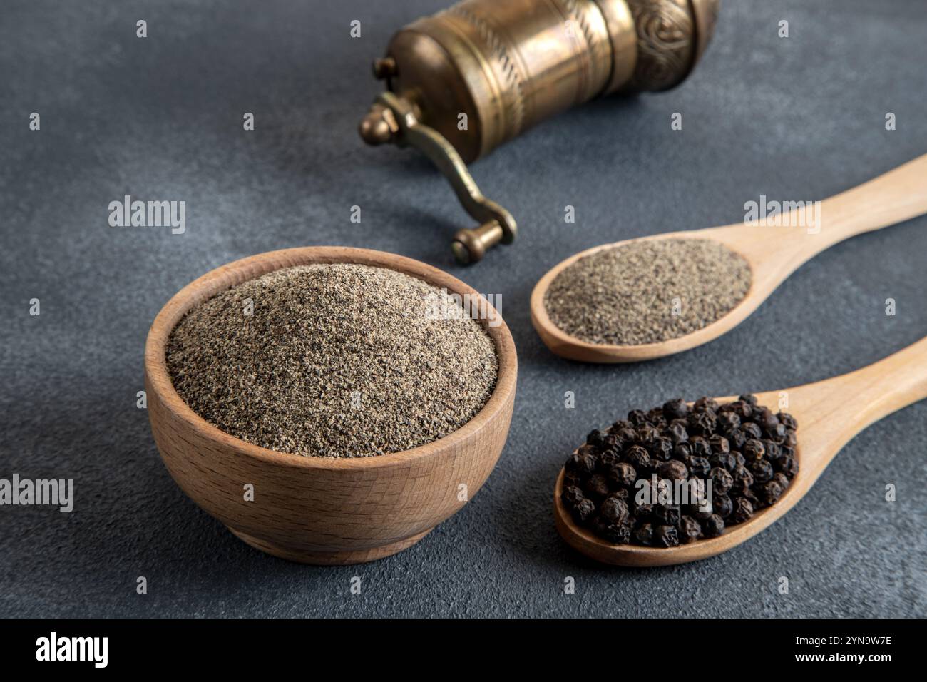 Schwarze Pfeffer, gemahlener schwarzer Pfeffer und Metallmühle auf schwarzem Hintergrund Stockfoto