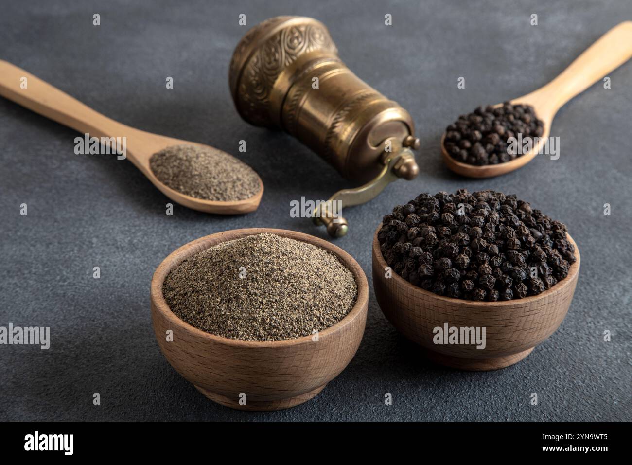 Schwarze Pfeffer, gemahlener schwarzer Pfeffer und Metallmühle auf schwarzem Hintergrund Stockfoto
