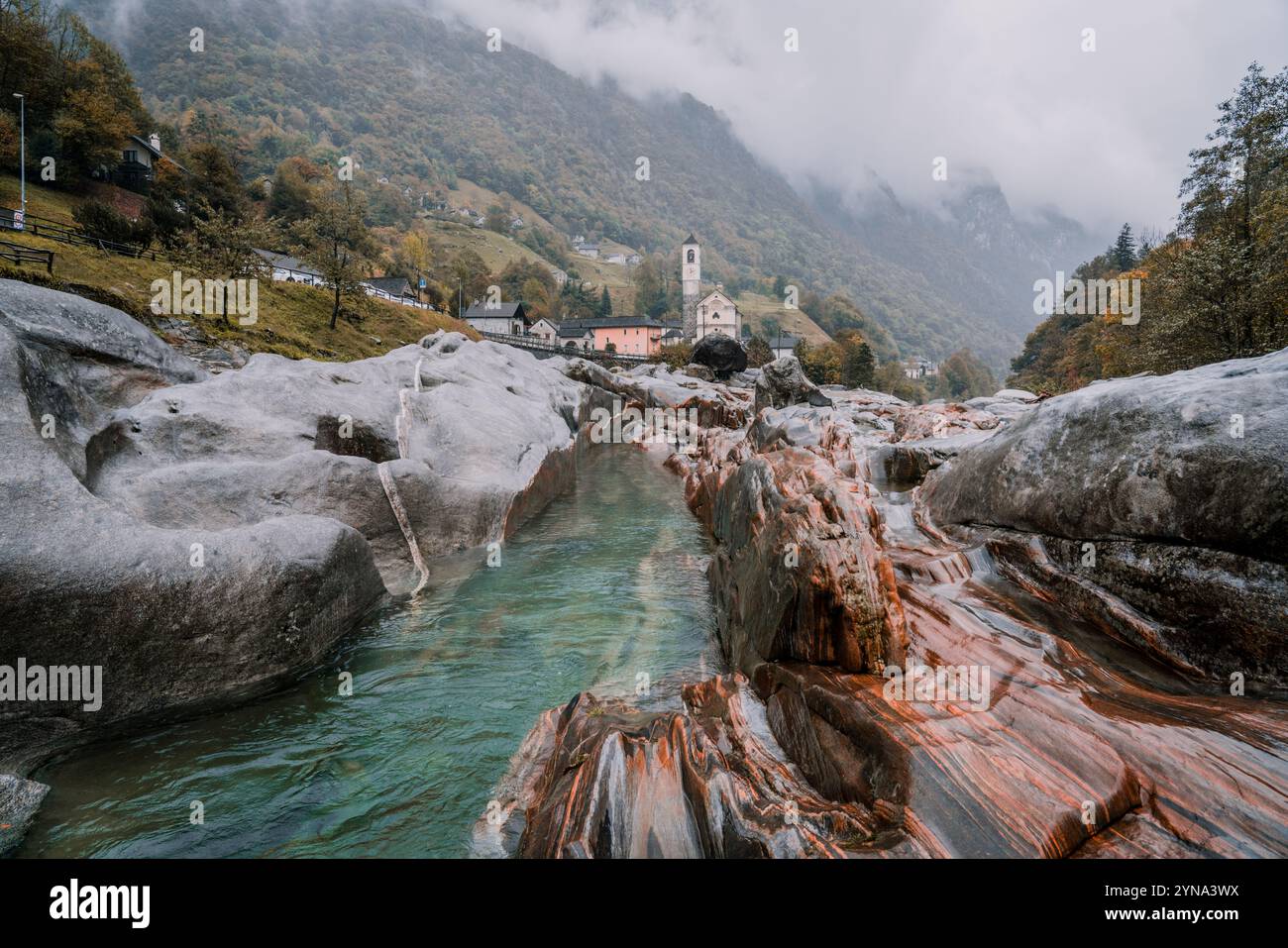 Eine regnerische Herbstlandschaft mit lebhaftem Laub umgibt einen sanft fließenden Fluss, der alle von weichem, geheimnisvollem Nebel umhüllt ist Stockfoto